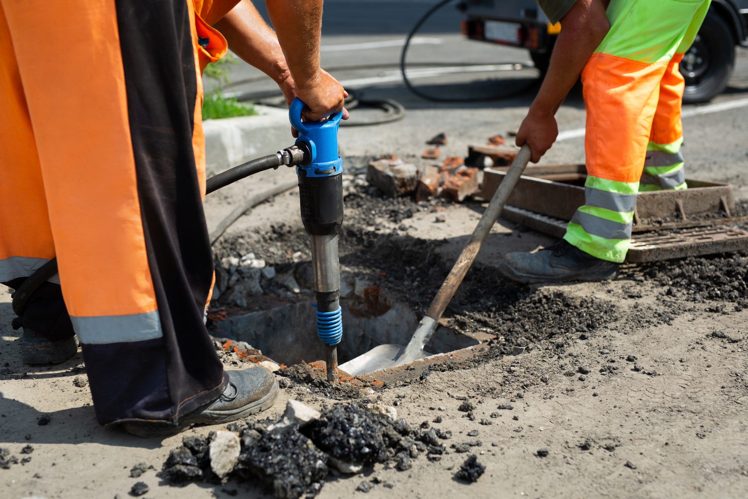 A road worker is dismantling street asphalt and old drainage with a jackhammer