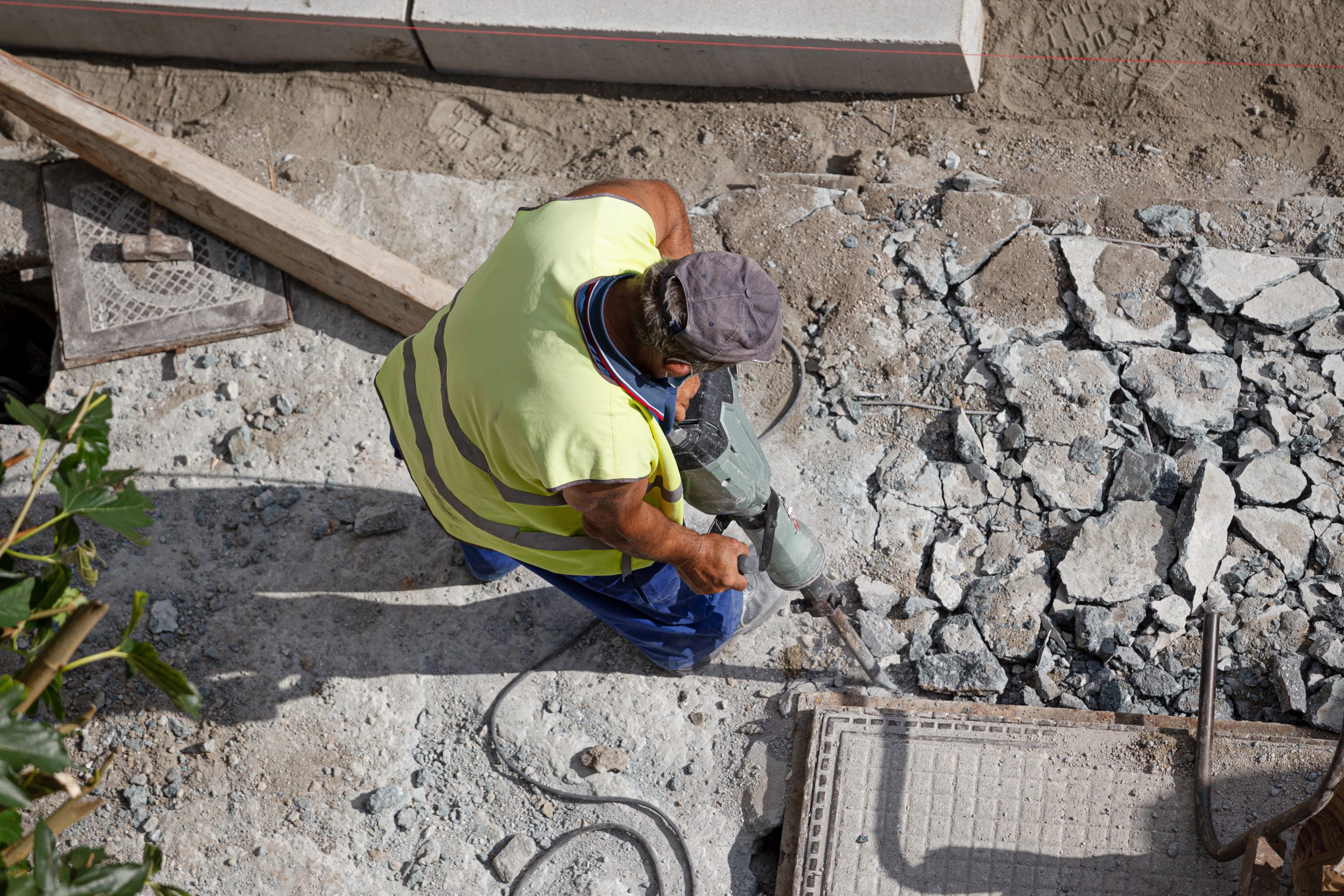 Construction worker with jackhammer drilling concrete on sidewalk. City Maintenance concept