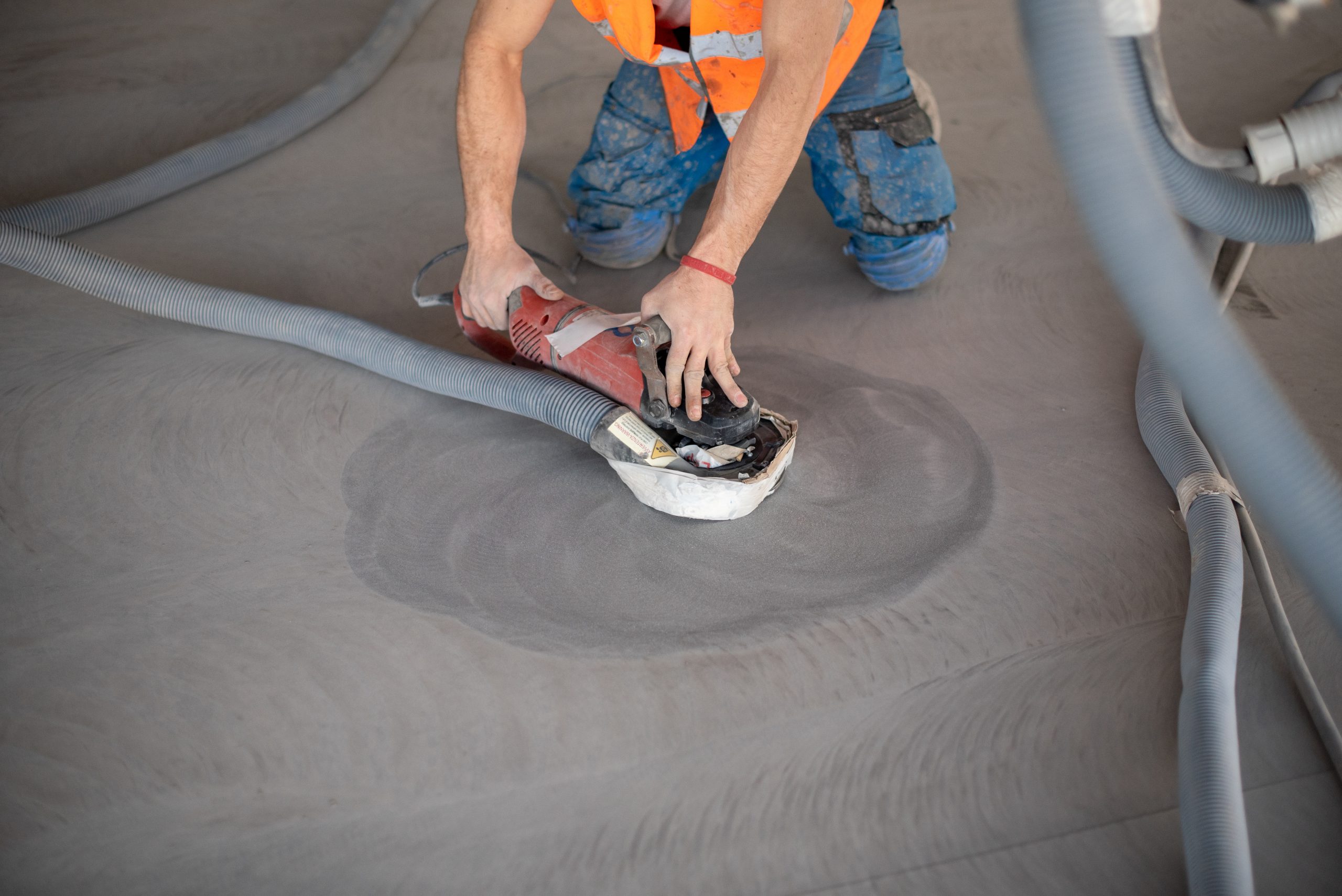 Worker working on the floor of an industrial building. Construction worker producing grout and finishing wet concrete floor.